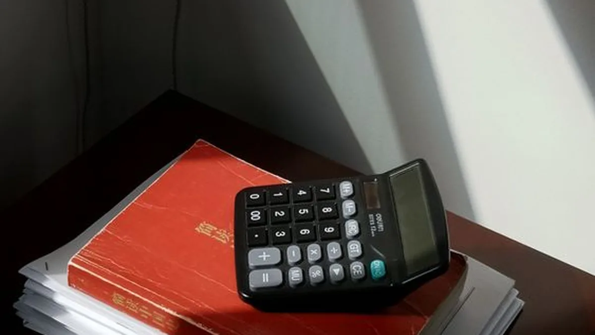 Une calculatrice noire repose sur un livre rouge posé sur une pile nette de papiers, dans la lumière du soleil : le tri des justificatifs avant la déclaration.