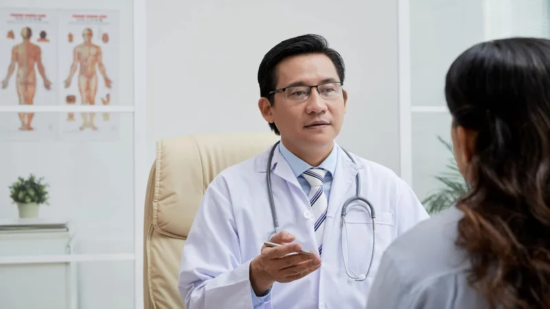 Un médecin en blouse blanche, stéthoscope au cou, explique quelque chose à sa patiente dans son cabinet.