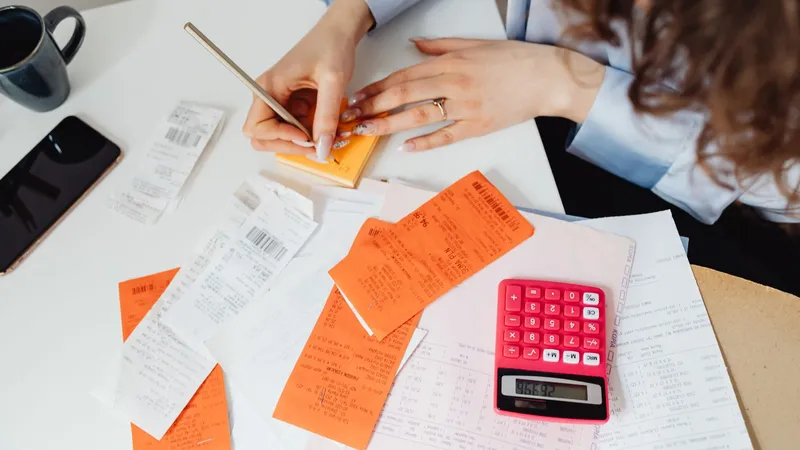 Des mains trient des tickets et des billets sur un bureau, avec une calculatrice rouge.