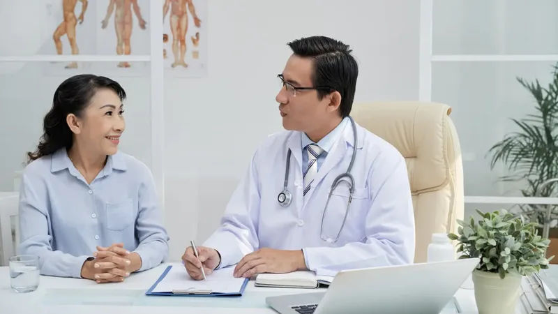 Une patiente souriante discute avec son médecin en blouse blanche, assis à son bureau avec un ordinateur portable.