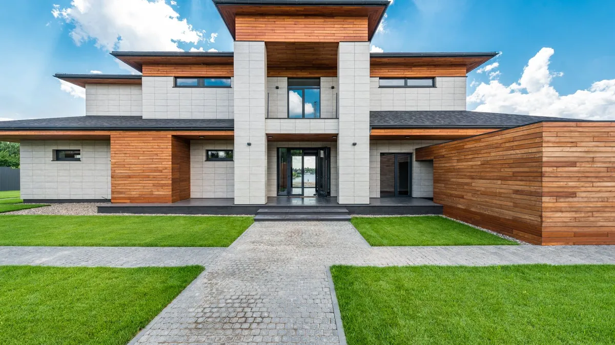 Une maison contemporaine à toit plat, façade bois et pierre, devant une pelouse verte.