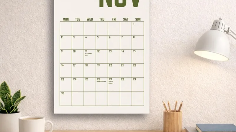 Un calendrier mensuel accroché au mur au-dessus d'un bureau, lampe et pot à crayons posés à côté.