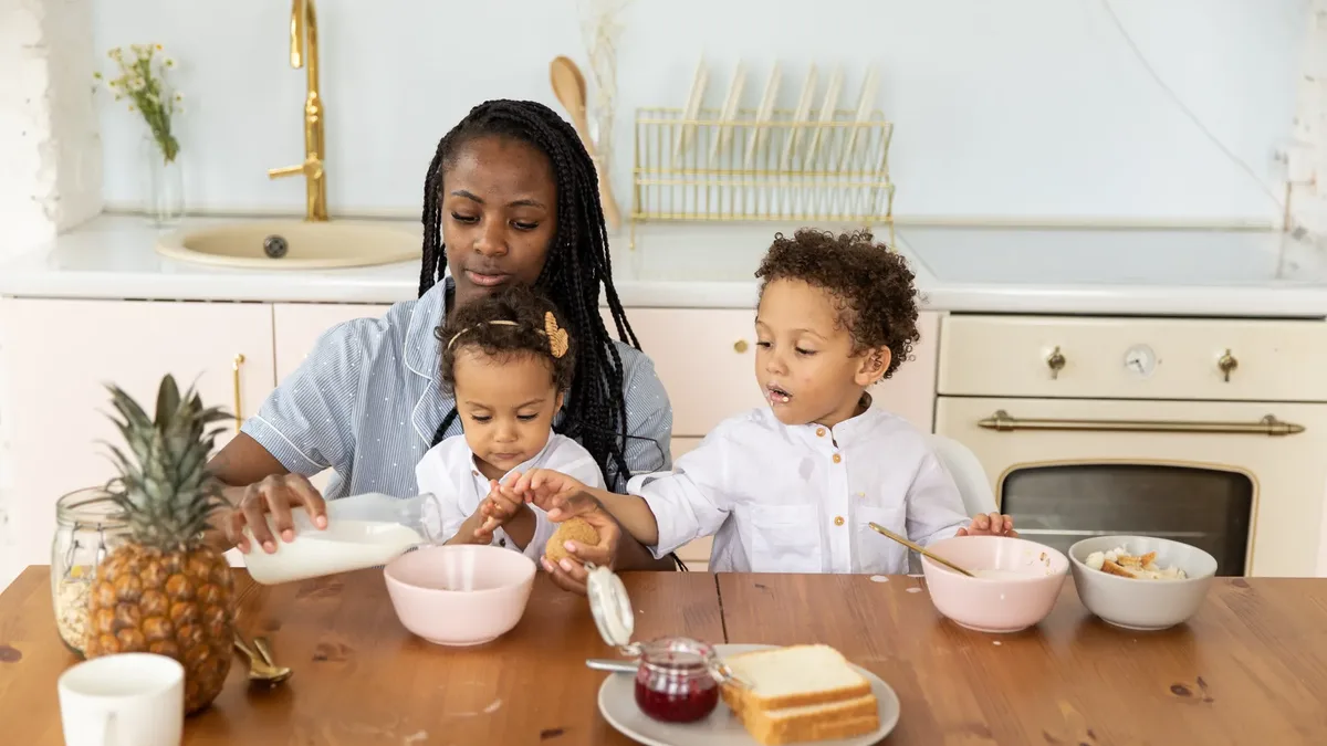 Une mère partage le petit-déjeuner avec ses deux enfants à la table de la cuisine familiale : le foyer dont la taille fixe le nombre de parts.
