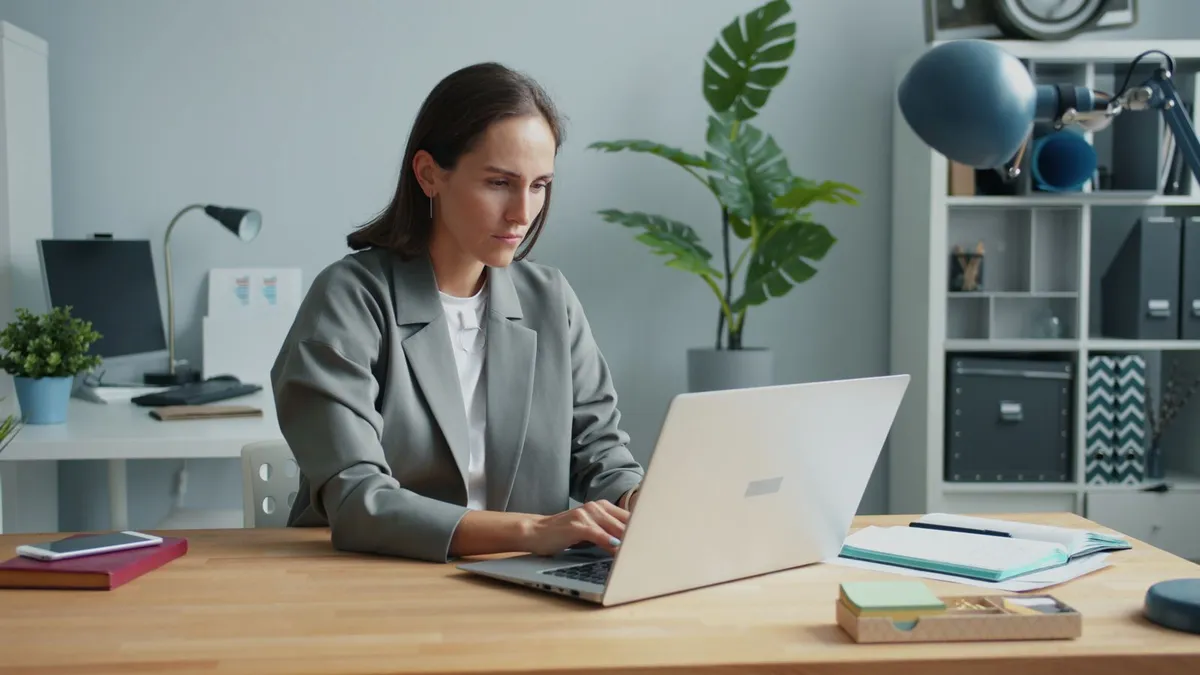 Une femme travaille sur son ordinateur portable dans un bureau moderne et lumineux, plantes vertes autour d'elle.