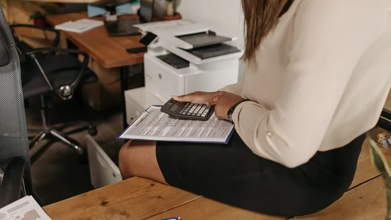 Une femme au bureau pose une calculatrice sur un document imprimé en tableau : comparer une offre de crédit ligne par ligne, TAEG compris.